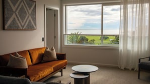 Un salon avec une grande fenêtre, un canapé, une table basse et une œuvre d’art accrochée au mur.
