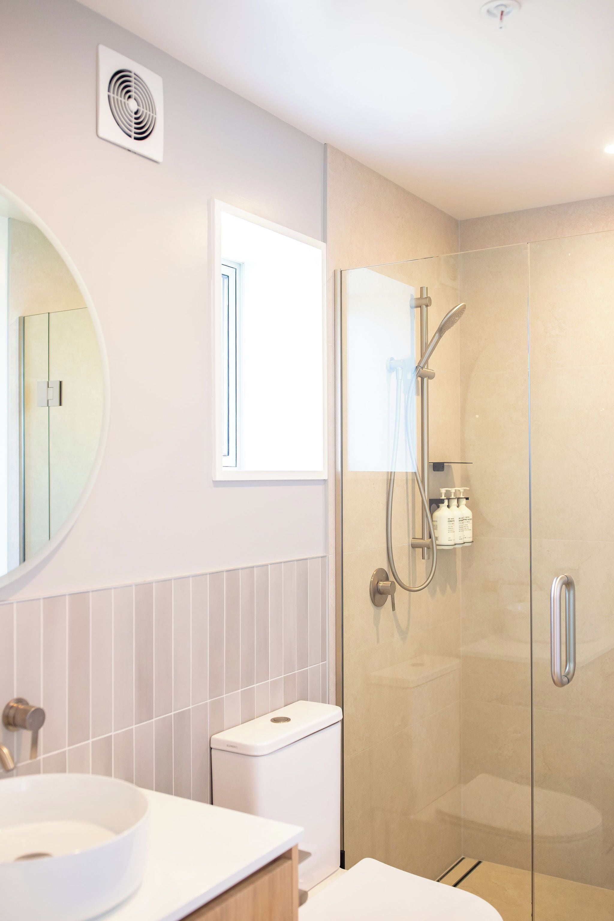 A modern bathroom with a glass-enclosed shower, a round mirror, and a white sink.