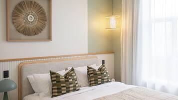 A neatly made bed with checkered pillows, a framed abstract artwork above it, and a bedside lamp.