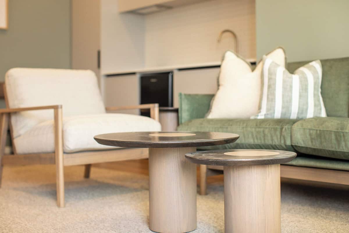 A modern living room with a green sofa, a white armchair, and two round wooden tables.