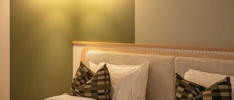 A bed with white bedding and checkered pillows, a headboard with a wooden trim, and a wall-mounted light fixture.