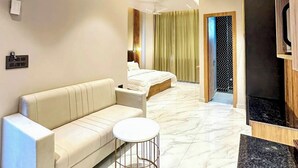 Een moderne hotelkamer met een bank, rond salontafeltje, plafondventilator en een bed met gordijnen.