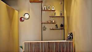 Een kamer met een houten spijlenbureau, wandplanken met diverse spullen, en een plafondventilator.