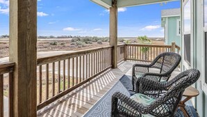 Eine überdachte Veranda mit Blick auf eine Wüstenlandschaft, Holzgeländern und Korbstühlen.