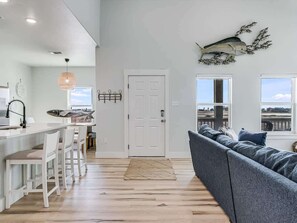 A modern kitchen with white bar stools, a large window, and a view of the outdoors. - Cove Harbor Beach House (Rockport)