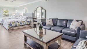 En moderne stue med en sofa, et sofabord, en seng med blomstret dynebetræk, et skrivebord med stol og et stort spejl.
