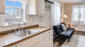 A kitchen with a sink, cabinets, a black leather sofa, and a window with curtains.
