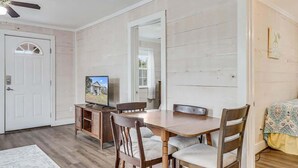 A dining area with a wooden table and chairs, a television on a cabinet, and a door leading to another room.