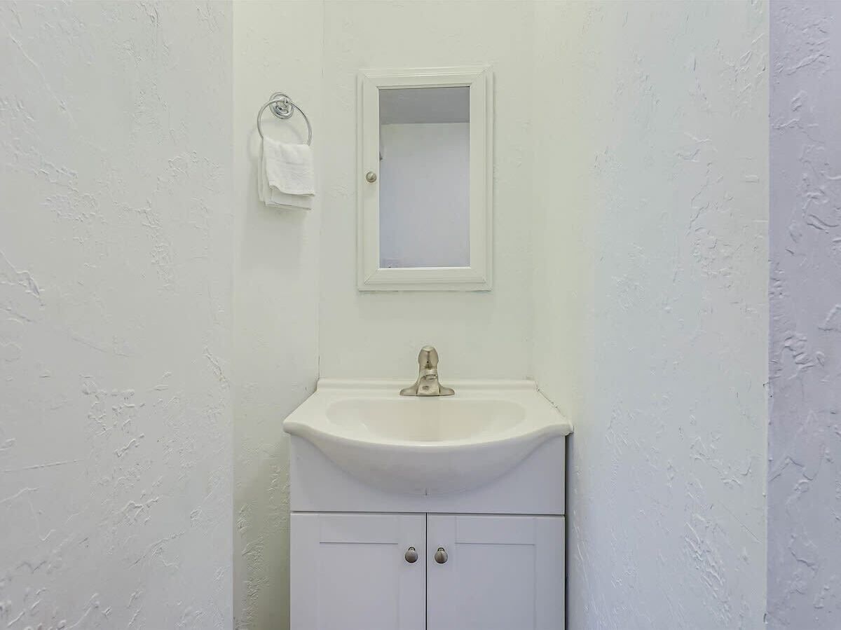 Un baño con un lavabo blanco, un espejo encima y una toalla colgada en un perchero.