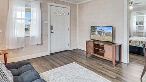 A living room with a wooden floor, a ceiling fan, a television, and a door.