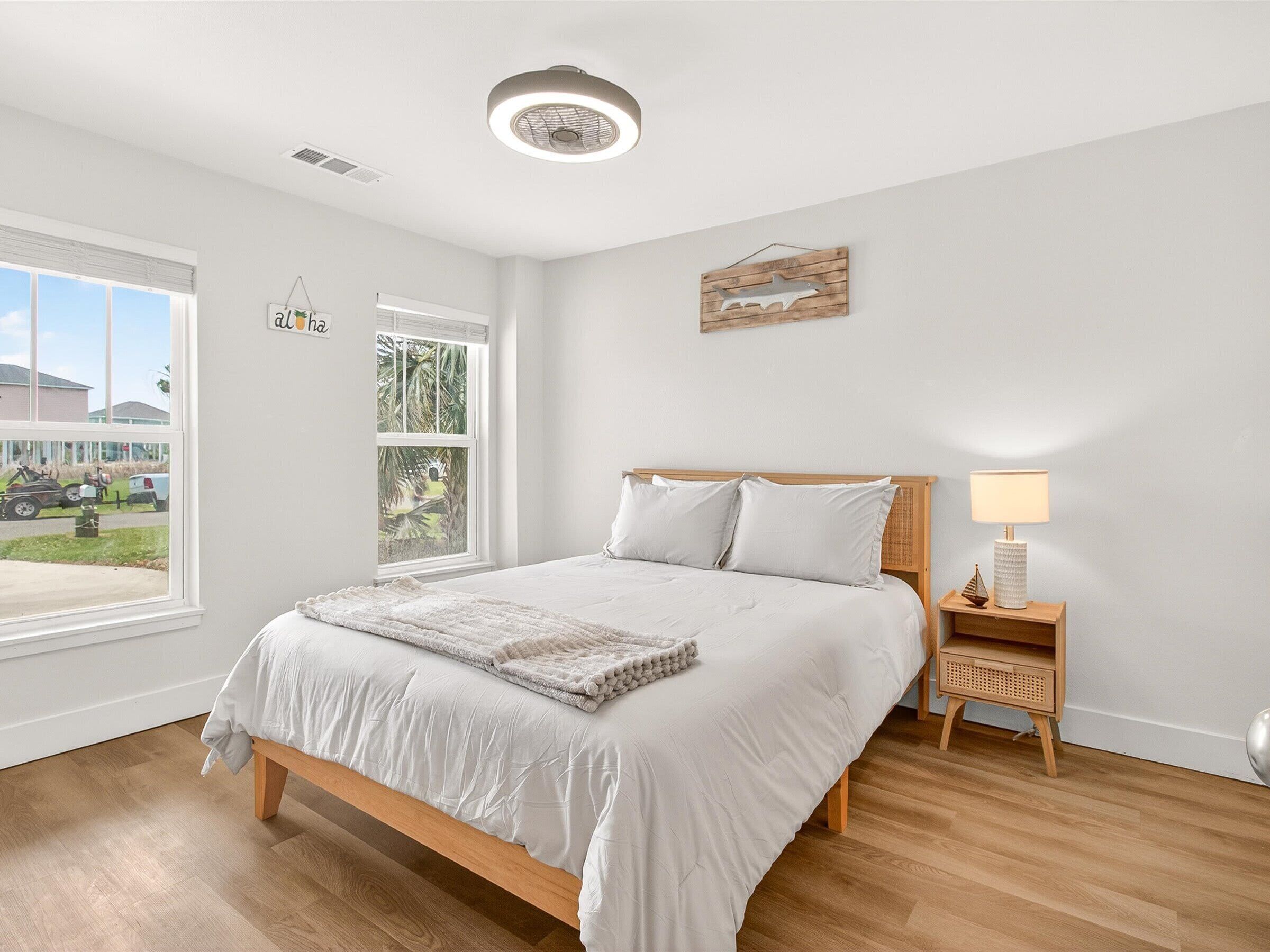 A bedroom with a bed, bedside table, lamp, and a window with a view of a street and buildings.
