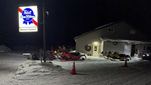 Een parkeerplaats bedekt met sneeuw, met een bord voor 'Pabst Blue Ribbon Beer' en een gebouw met een krans bij de deur.