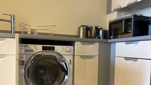 A compact kitchen with a built-in washer, microwave, and a coffee maker on the countertop. - 1 bed & 1 bath apartment large balcony - 10 min walk from new street station (Birmingham)