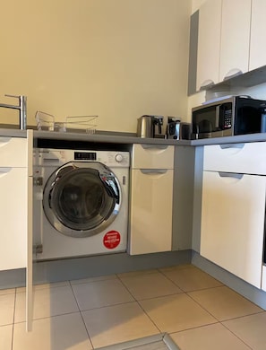 A compact kitchen with a built-in washer, microwave, and a coffee maker on the countertop. - 1 bed & 1 bath apartment large balcony - 10 min walk from new street station (Birmingham)