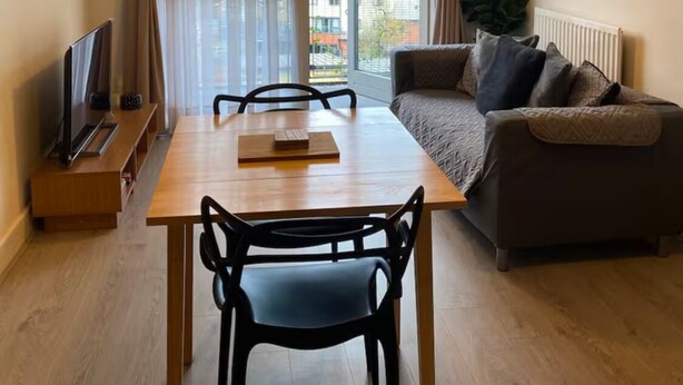 A modern living room with a wooden dining table, black chairs, a sofa, and a large window with curtains. - 1 bed & 1 bath apartment large balcony - 10 min walk from new street station (Birmingham)