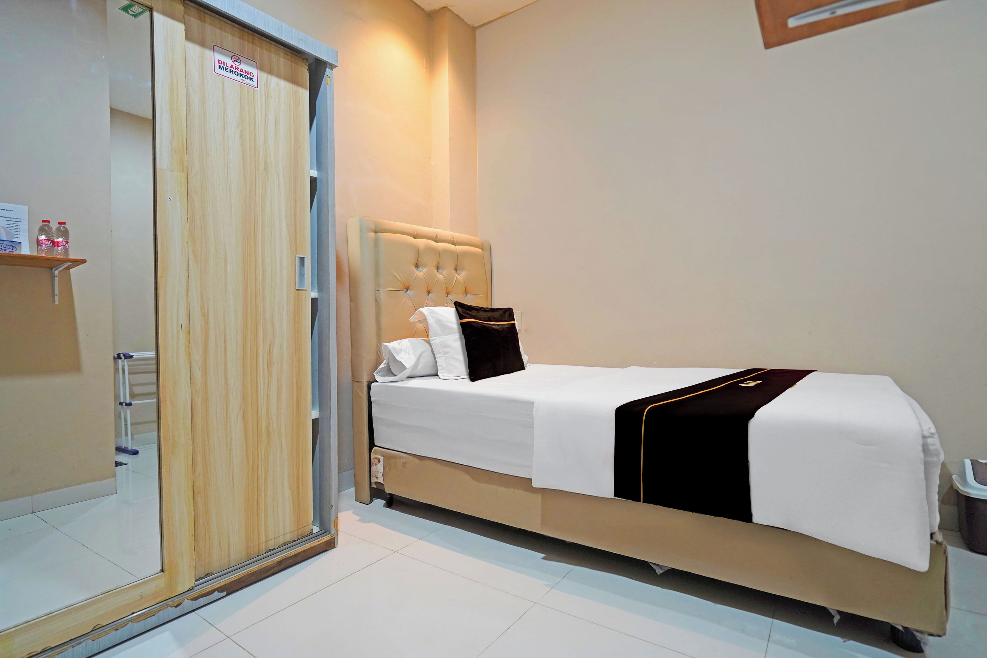 A hotel room with a bed, a wooden wardrobe, and a small shelf with bottles.