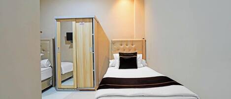 A hotel room with a bed, a wooden wardrobe, and a mirror.