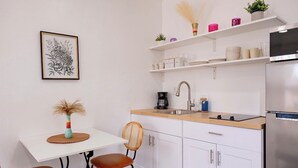 A compact kitchen with white cabinets, a stainless steel refrigerator, a coffee maker, and a small dining table with chairs. - The Lovely Gem 6 miles to Siesta Key Paradise (Sarasota)