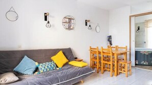 A modern living room with a grey sofa, yellow cushions, a wooden dining table, and wall-mounted light fixtures.