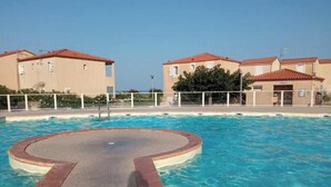 A swimming pool with a circular design, surrounded by a white fence, with buildings in the background.