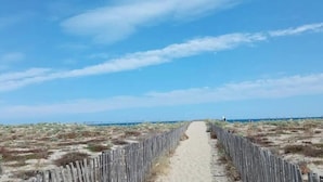 A sandy pathway flanked by wooden fences leading to a beach.