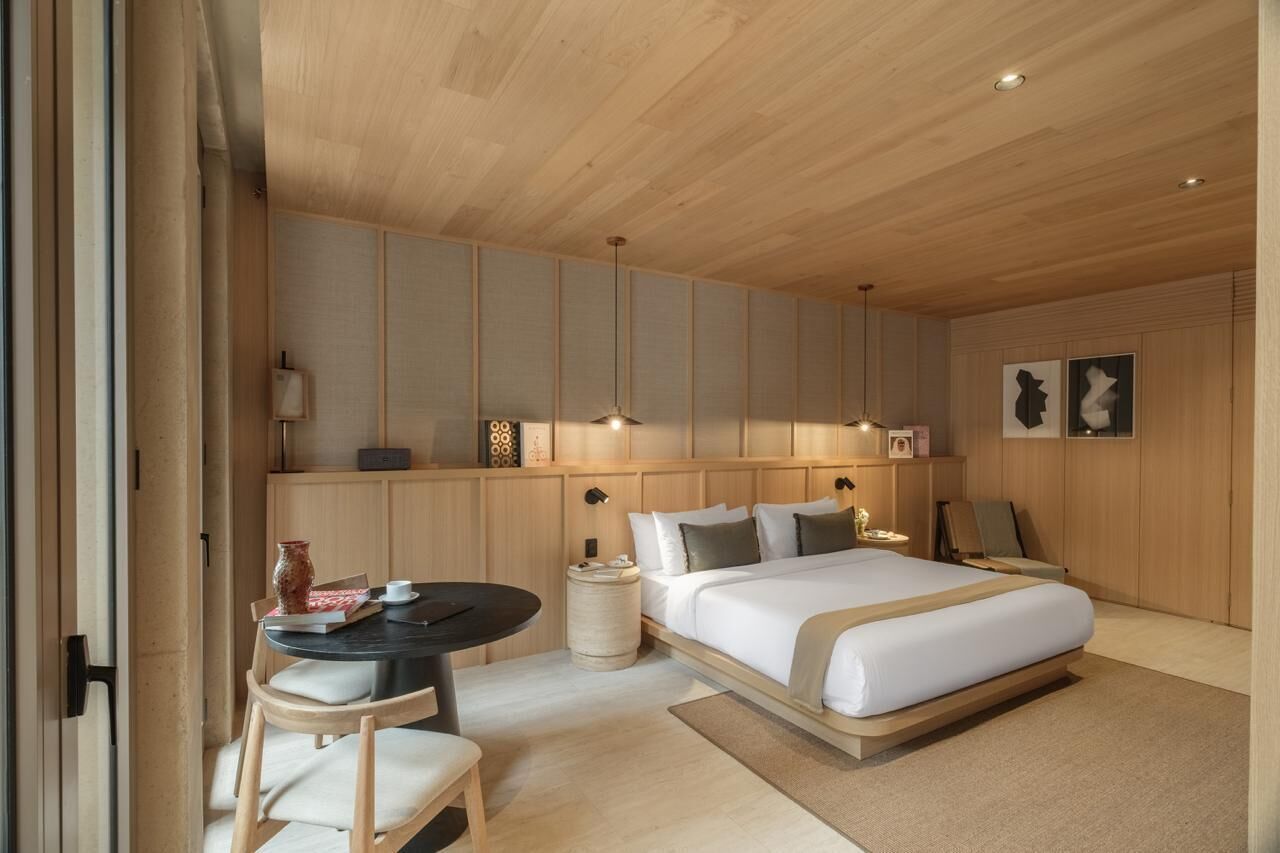 Un dormitorio moderno con una cama, mesitas de noche, una pequeña mesa con sillas y obras de arte en las paredes.