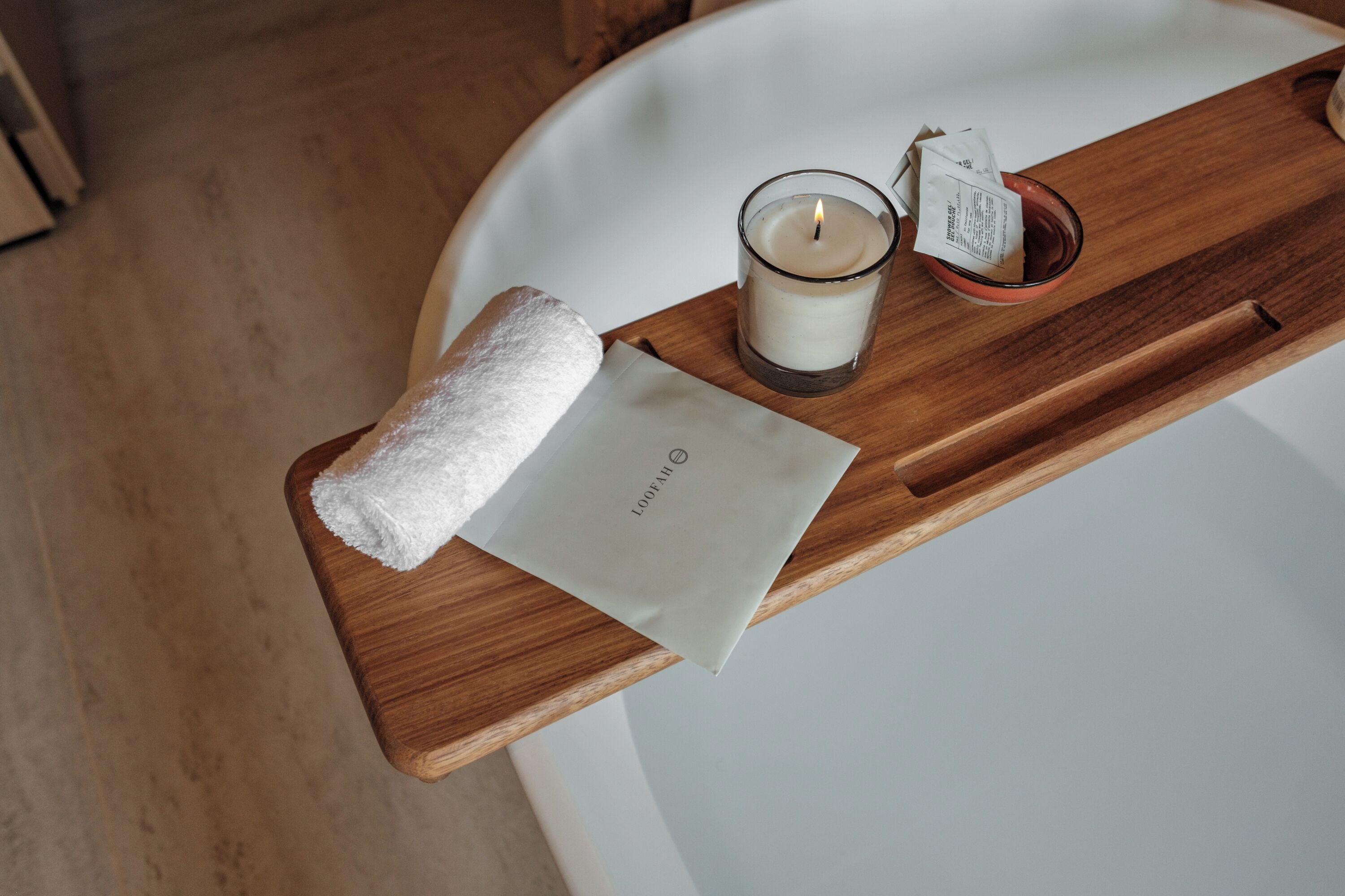 Un plateau en bois avec une serviette blanche, une bougie et une boîte de mouchoirs, posés sur le comptoir d’une salle de bain.