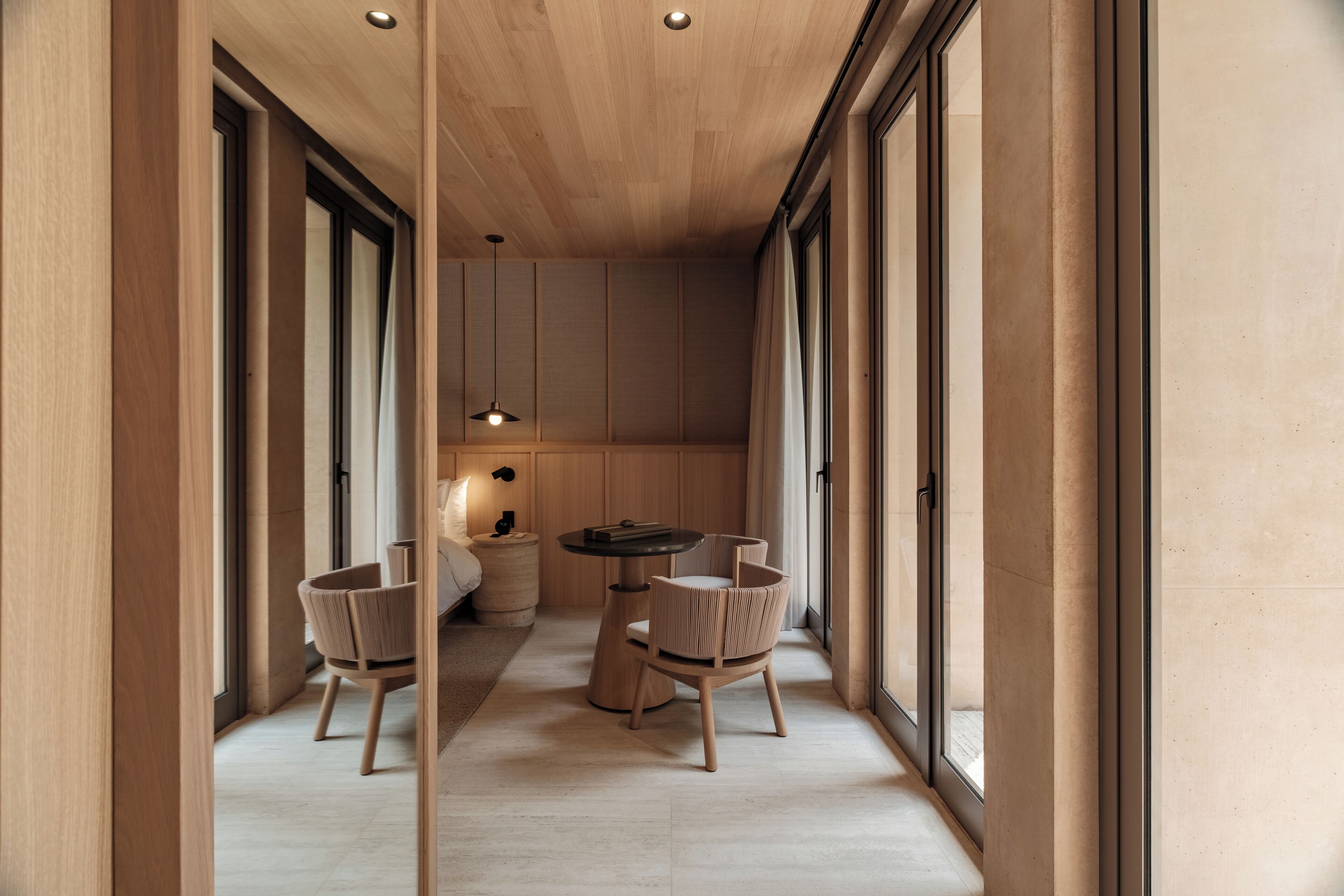 Un interior moderno con techo de madera, ventanas amplias, una mesa redonda y dos sillas.