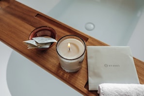 Un plateau en bois avec une bougie allumée, un verre d’eau, un petit bol rempli de mouchoirs et une serviette blanche ornée d’un logo.