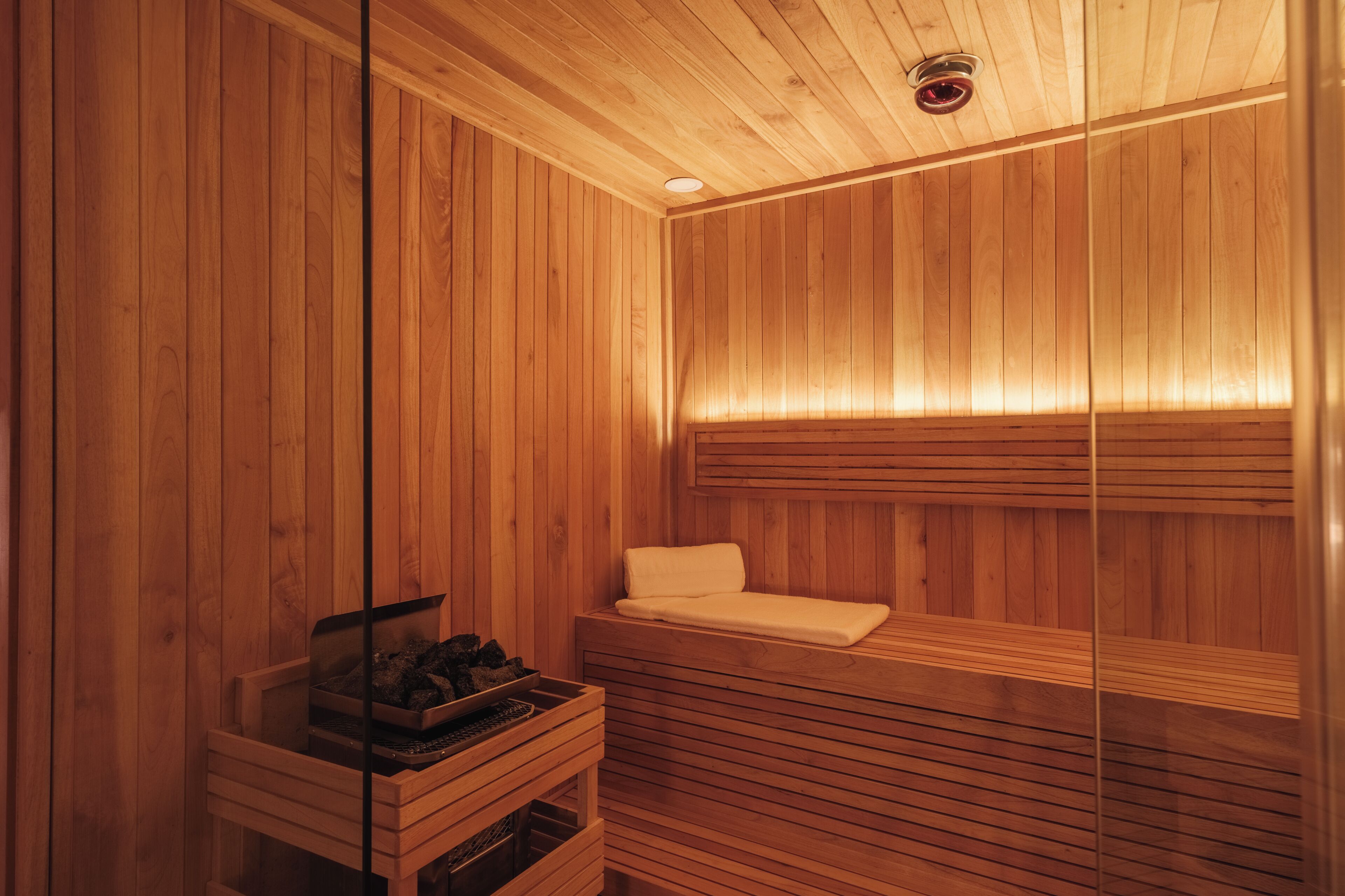 Una sauna de madera con un banco, un banco con una toalla y un armario de madera con objetos.