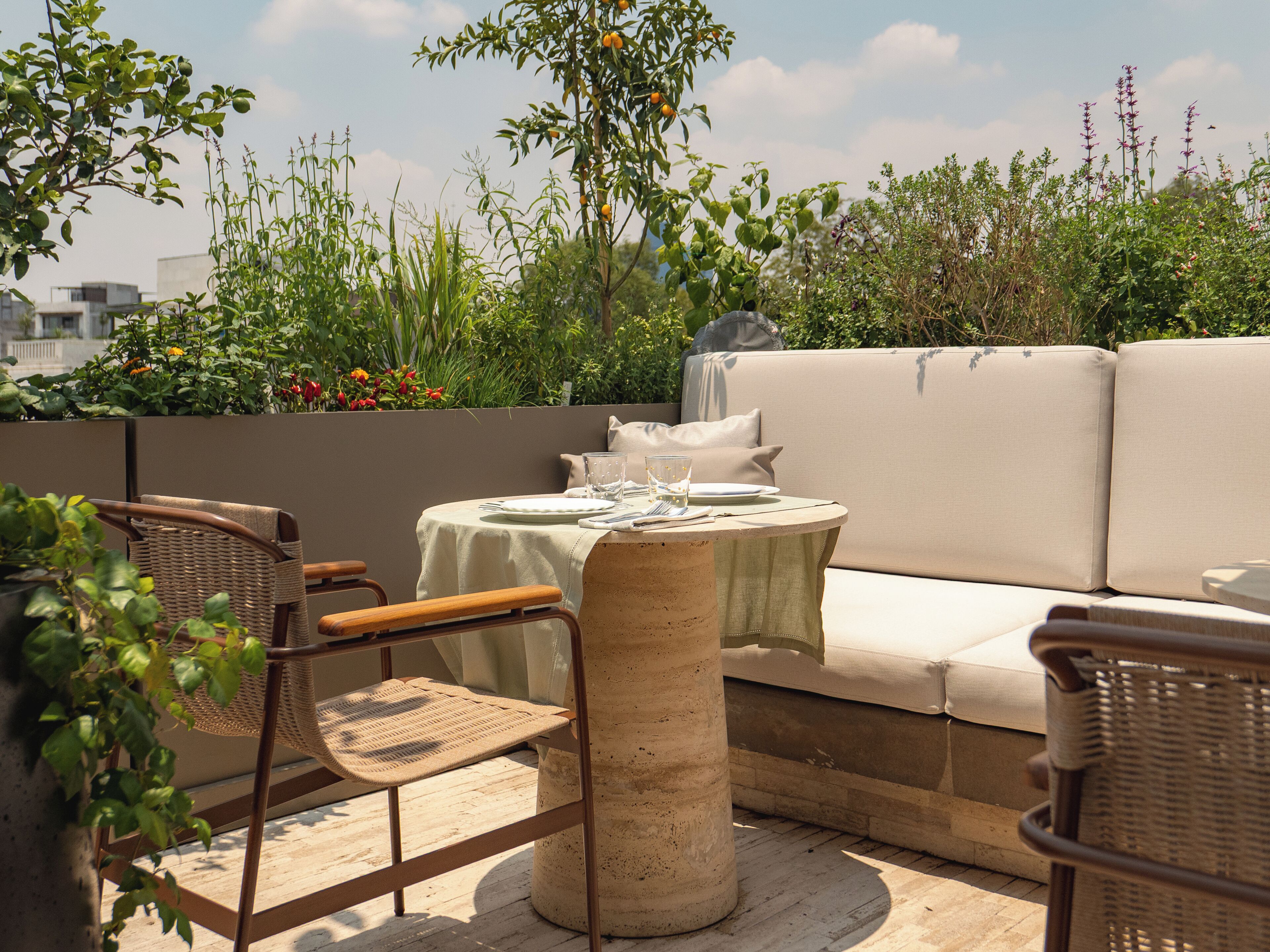 An outdoor seating area with a round table, two wicker chairs, a beige sofa, and a potted plant.