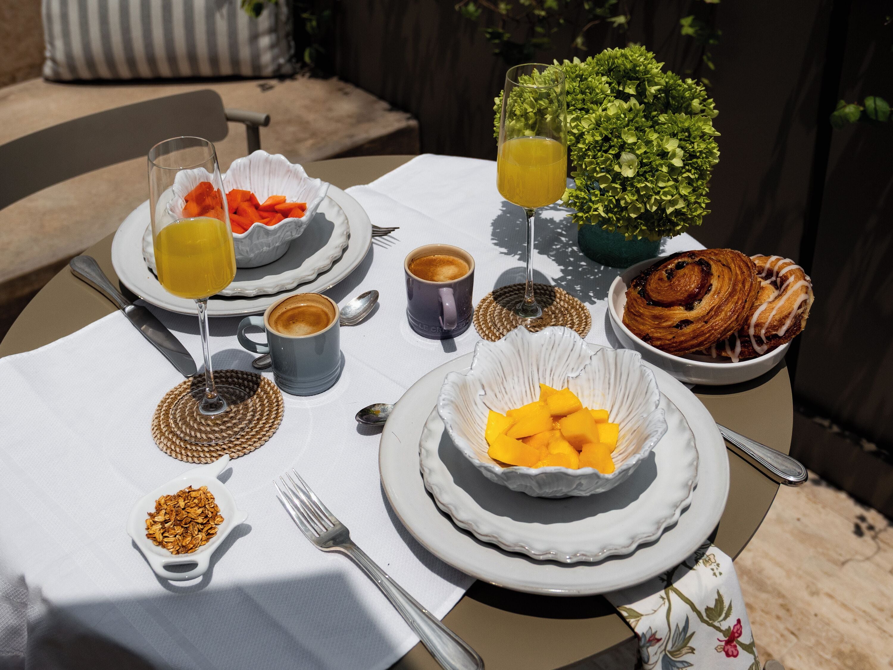 A table set with plates, bowls, a glass of juice, a coffee cup, a pastry, and a small plant.