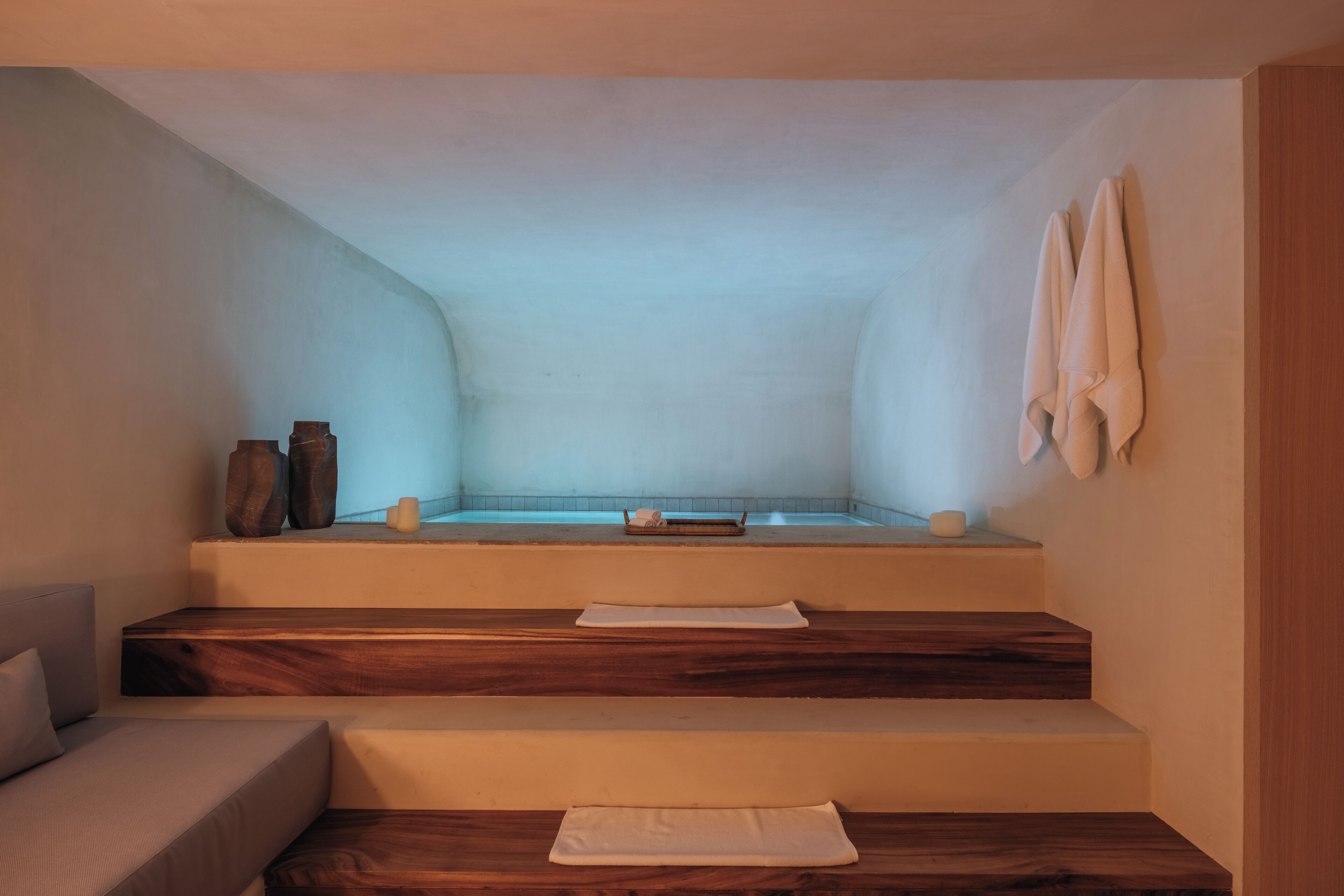 Un cuarto de spa con una bañera, escalones de madera, una toalla y jarrones decorativos.
