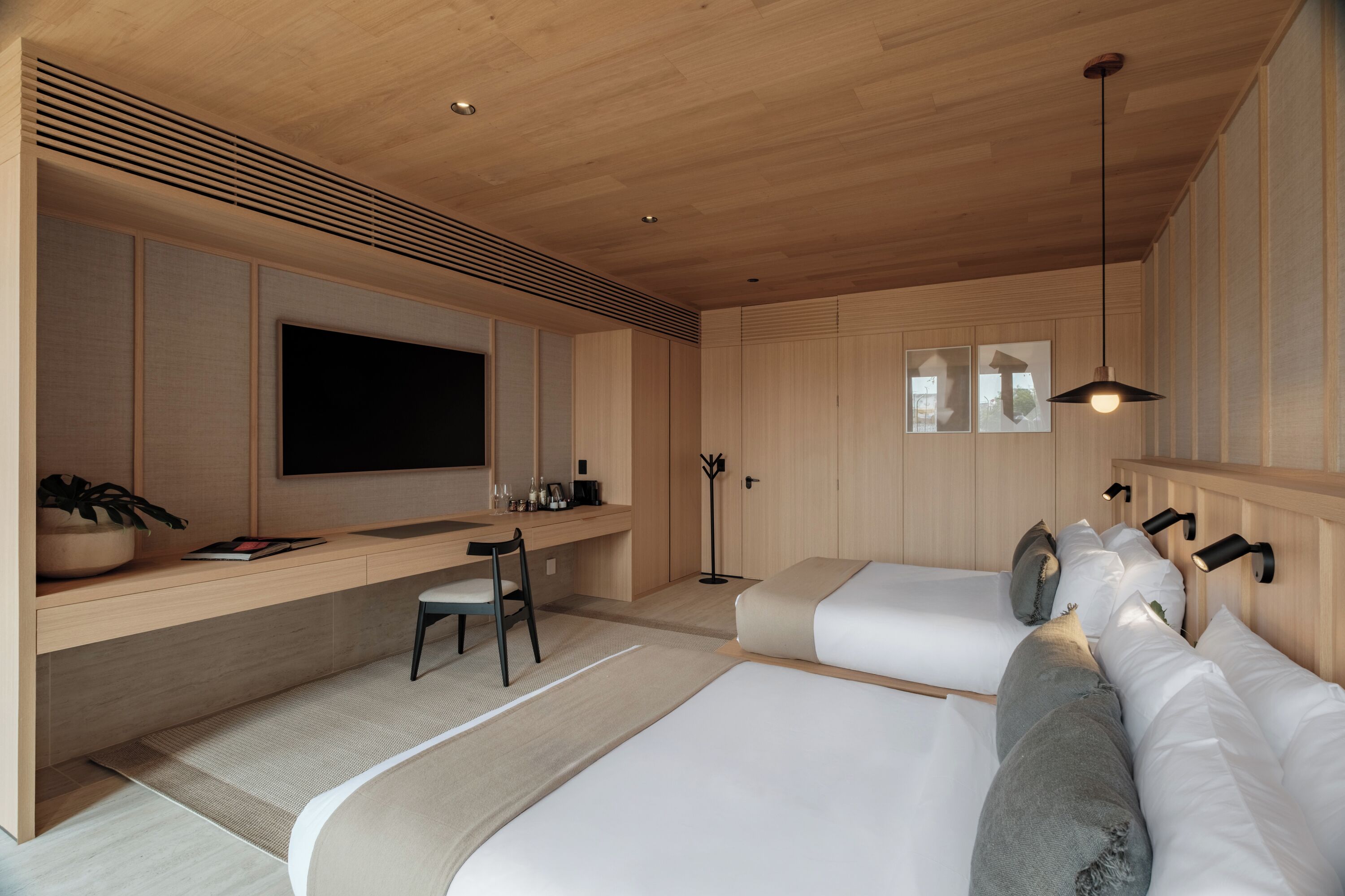 Un dormitorio moderno con techo de madera, un televisor de pantalla plana, un escritorio con silla, dos camas y una mesita de noche.