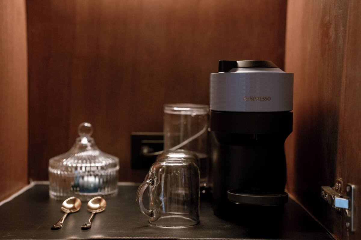 Una cafetera, una taza de vidrio, una jarra de vidrio y dos cucharas sobre una superficie oscura.