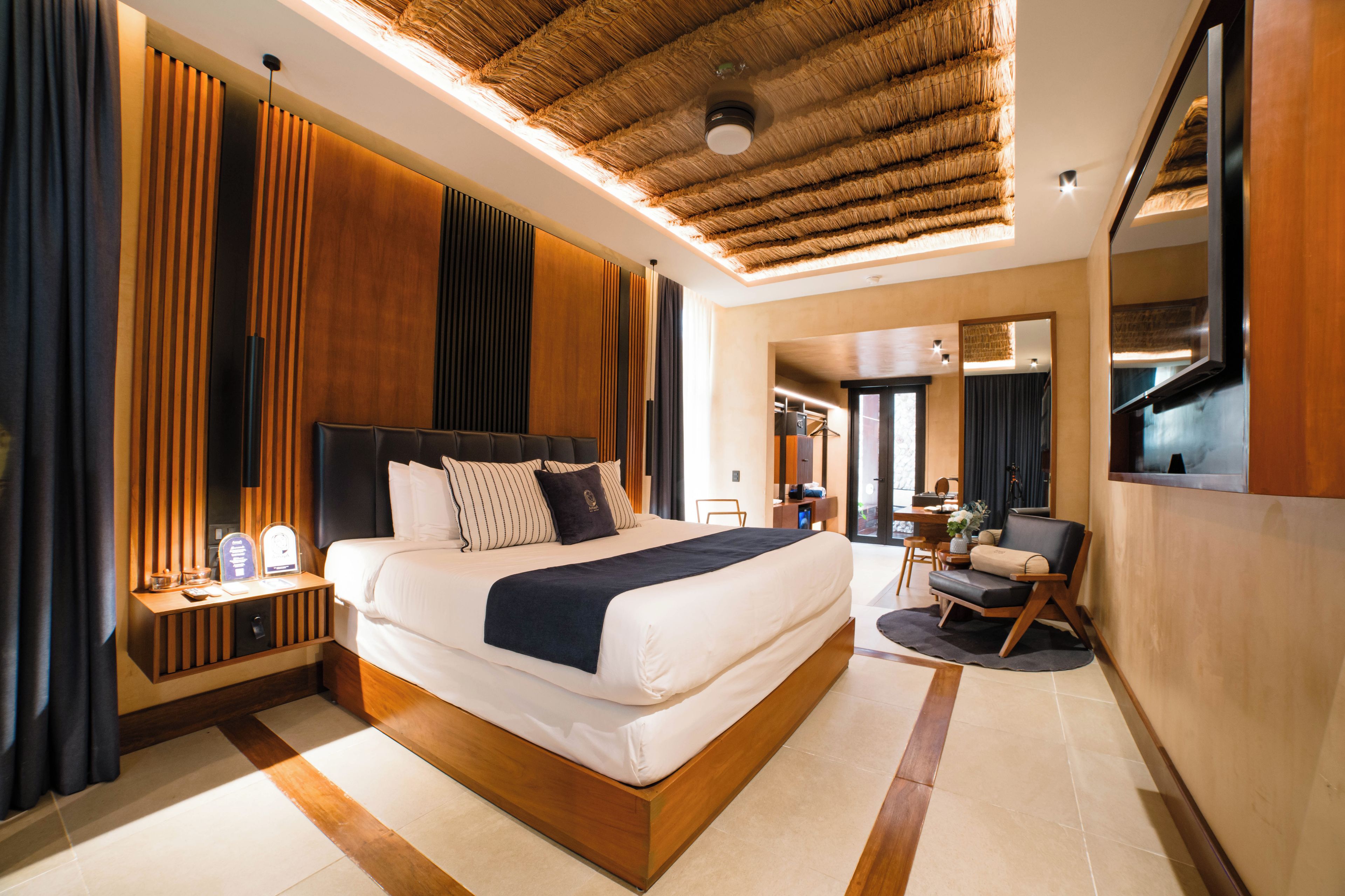 A modern hotel room with a large bed, wooden headboard, and a ceiling with a thatched design.