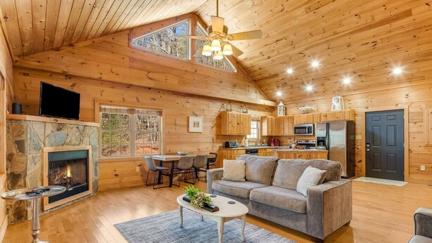 A cozy cabin interior with a stone fireplace, wooden floors, a dining area, and a kitchen. - NEW CABIN!-Pet Friendly-Babbling Brook-Private Lake-Grill (Lake Lure)