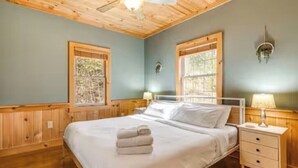 A bedroom with a bed, two bedside tables, a ceiling fan, and two windows with wooden frames. - NEW CABIN!-Pet Friendly-Babbling Brook-Private Lake-Grill (Lake Lure)