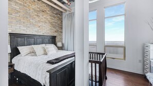 Ein Schlafzimmer mit Backsteinwand, einem hölzernen Bett, einem Babybett und großen Fenstern.