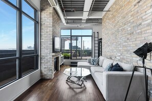 A modern living room with a fireplace, large windows, a white sofa, and a glass coffee table.