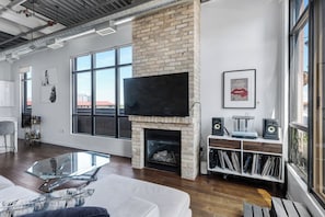 A modern living room with a fireplace, large windows, a flat-screen TV, and a music stand.