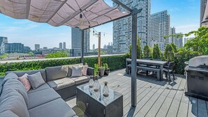 Eine Dachterrasse mit einer Sitzecke, Tisch, Grill und Sonnenschirm.
