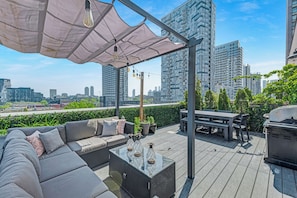 A rooftop patio with a sofa, table, grill, and umbrella.