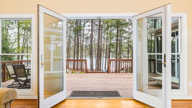 An open sliding glass door leading to a wooden deck with a view of tall trees. - Lakefront, Dock, Kayaks, Games, Firepit, Fireplace (Littleton)