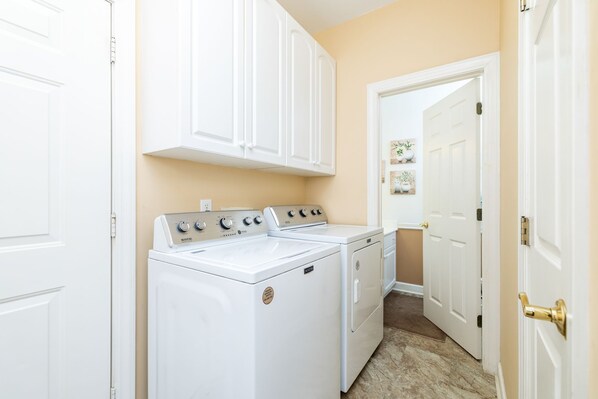 A laundry room with a washer and dryer, white cabinets, and a door leading to another room.