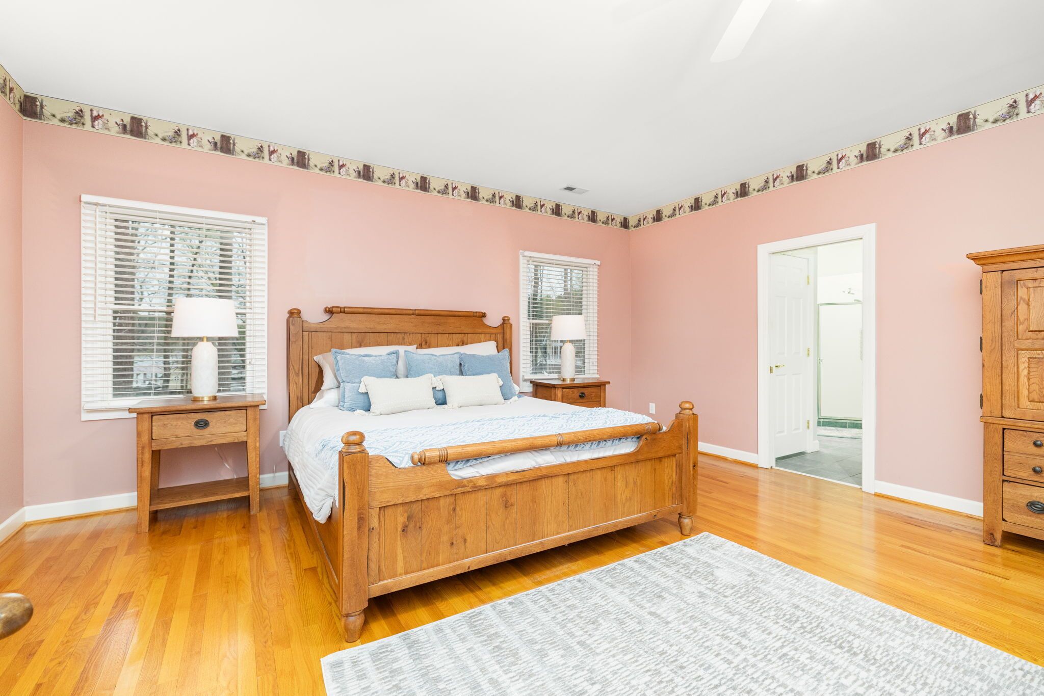 Un dormitorio con una cama de madera, dos mesitas de noche con lámparas, un mueble auxiliar y una alfombra estampada.
