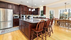 A spacious kitchen with dark wood cabinets, stainless steel appliances, and a central island with bar stools. - Lakefront, Dock, Kayaks, Games, Firepit, Fireplace (Littleton)