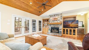 A spacious living room with a fireplace, wooden ceiling, and a large TV. - Lakefront, Dock, Kayaks, Games, Firepit, Fireplace (Littleton)