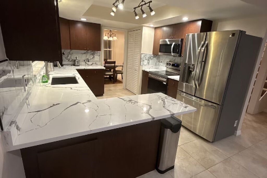 A modern kitchen with a marble countertop, stainless steel appliances, and a dining area with a chandelier.