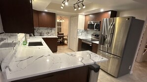 Een moderne keuken met een marmeren aanrecht, roestvrijstalen apparatuur en een eethoek met een kroonluchter.
